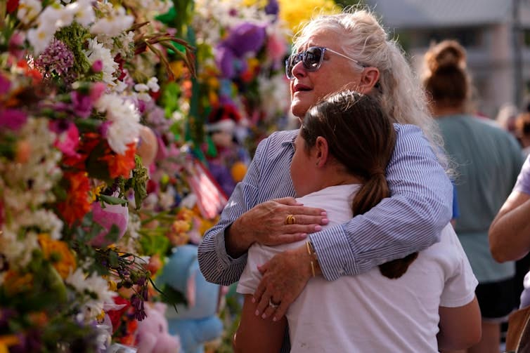 A grandmother embraces a young woman in front of a wall of flowers. A grandmother embraces a young woman in front of a wall of flowers.