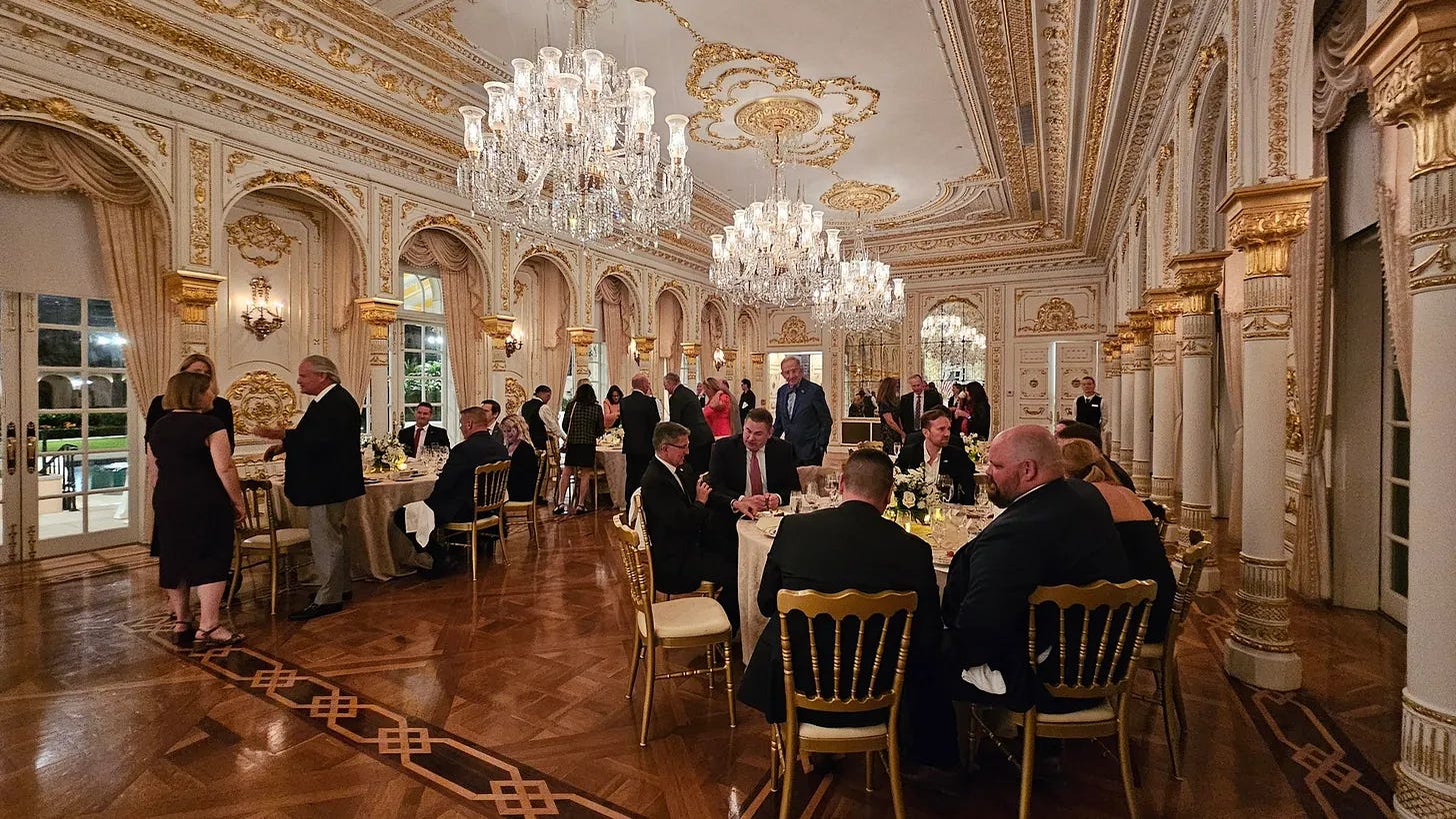 Photo from a Mar-a-Lago fundraiser for Brenna Bird showing guests seated and standing in an ornate ballroom with chandeliers and dining tables.