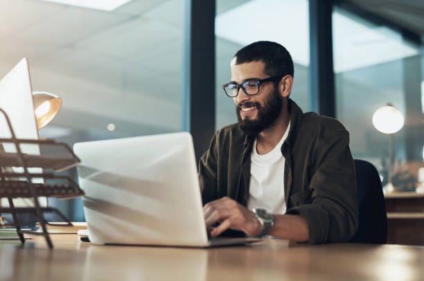Put more in, get more out Shot of a young businessman using a laptop during a late night in a modern office Website Design Company stock pictures, royalty-free photos & images