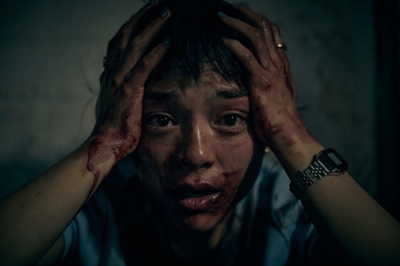 A still from the film "Saccharine." Actress Midori Francis holds her head in her hands, her face covered in what looks like blood.