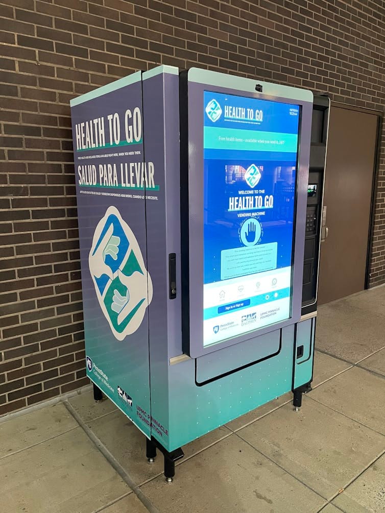 A teal and grey vending machine that says 'Health To Go' with large digital touchscreen on front
