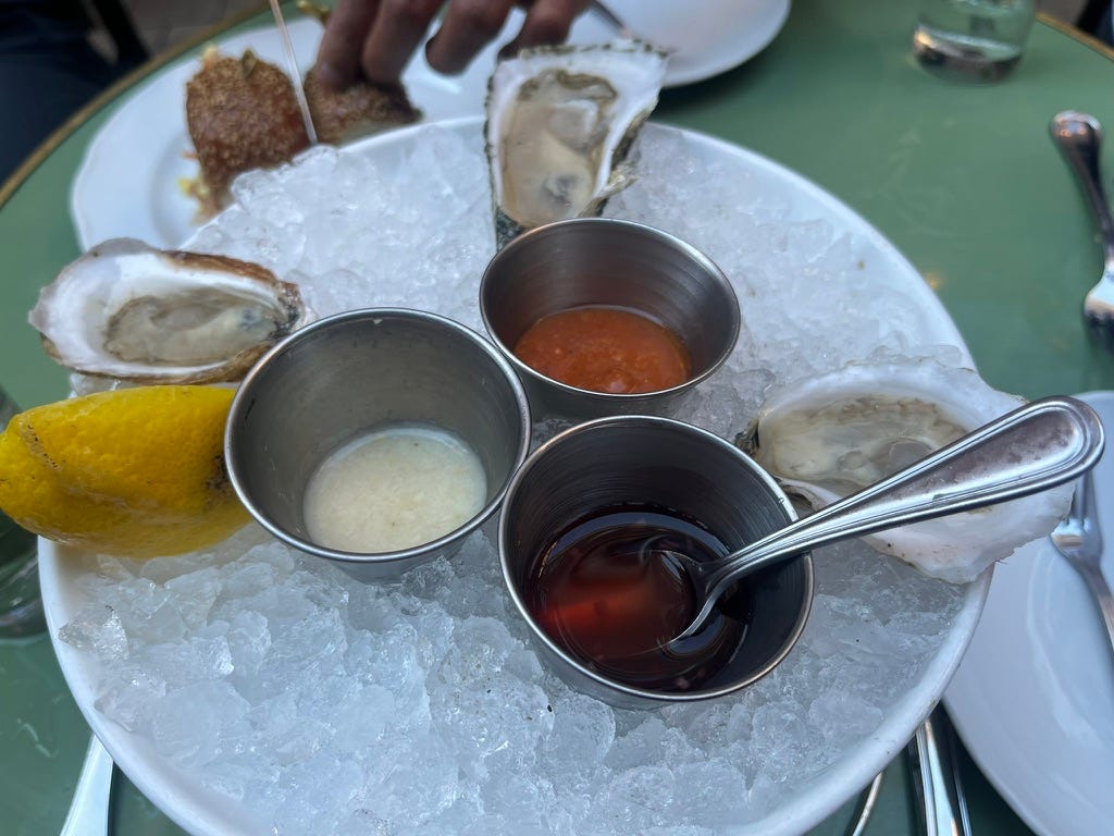 3 fresh oysters on a plate of ice, with a lemon wedge and 3 different sauces: white, orange, and brown