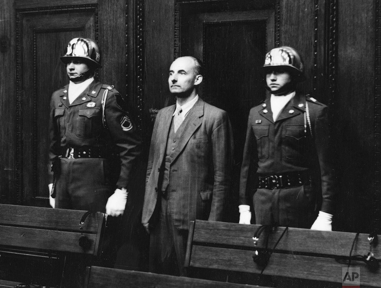 Defendant Hans Kehrl receives a 15-year sentence, flanked by U.S. Army honor guards Sgt. Thomas H. Andress and Pfc. Charles L. Scoarce, members of the 16th Infantry Regiment, during the Nuremberg trials.