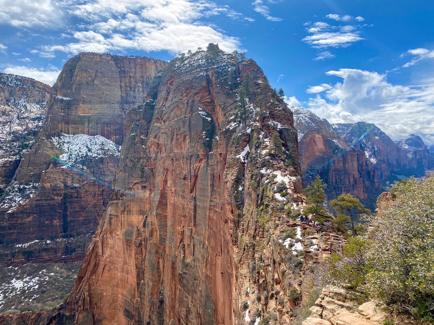 The red rock fin known as Angels Landing - one of the most epic hikes in the national parks - rises towards a blue sky.