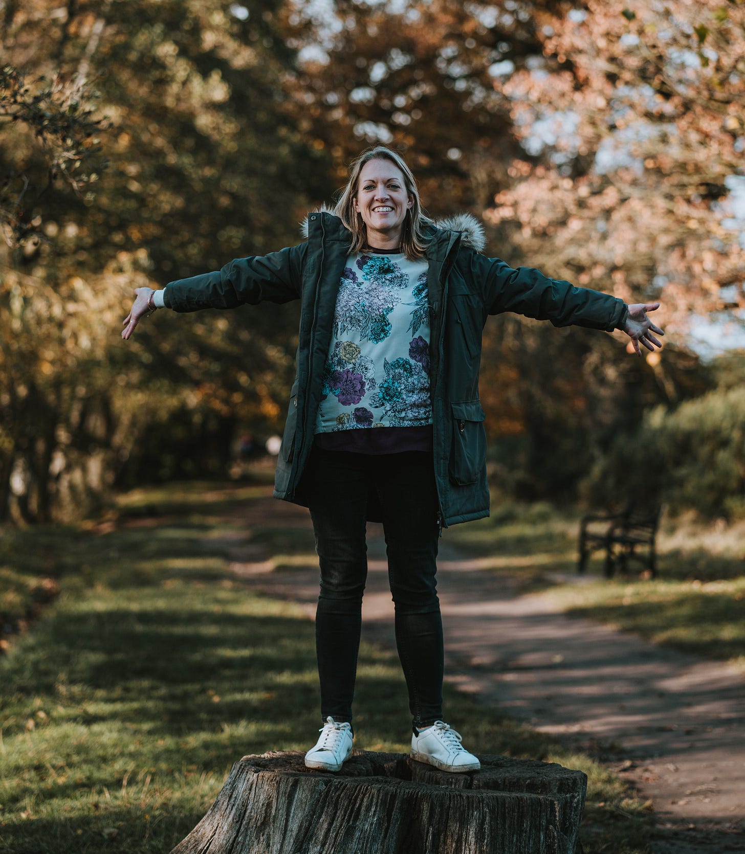 Photo of a woman smiling with arms held out wide in a wood