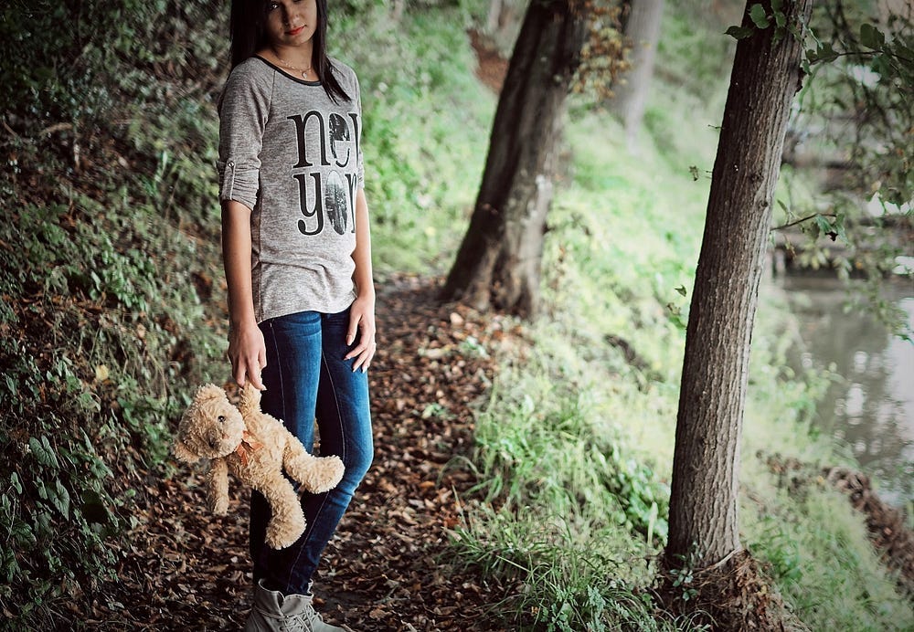 A pre-teen girl in the woods holding a teddy bear A pre-teen girl in the woods holding a teddy bear