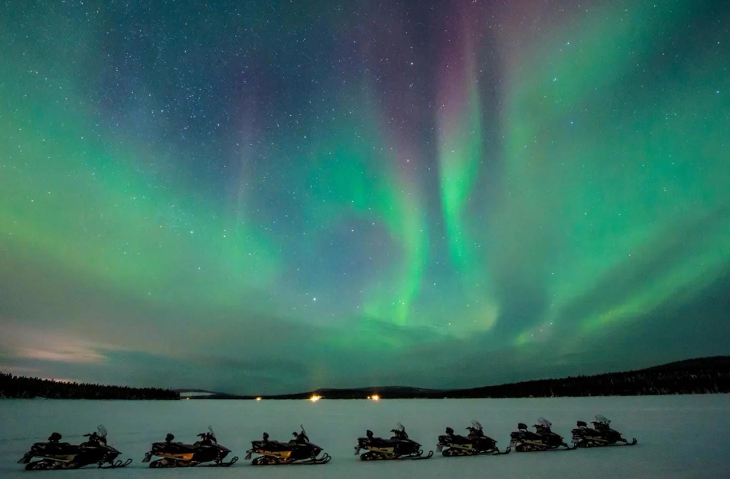 Snowmobiles parked in a snowy Arctic landscape at night near ICEHOTEL.