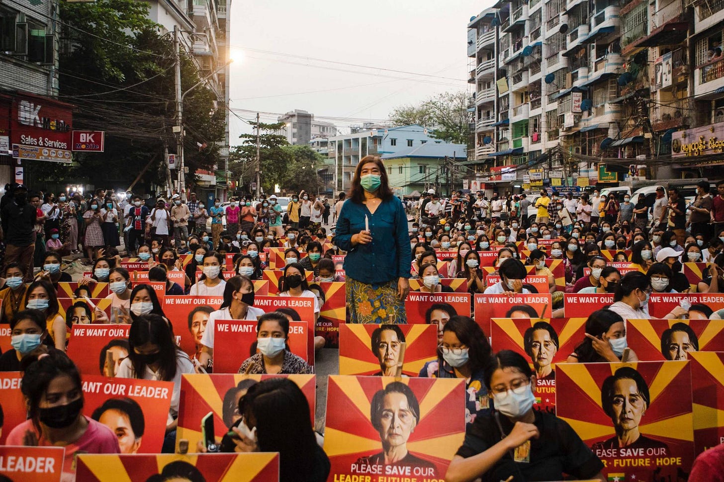 Protesters holding placards with the image of detained Myanmar civilian leader Aung San Suu Kyi sit along a street before a candlelight vigil during a demonstration against the military coup, in Yangon on March 12. | AFP-JIJI