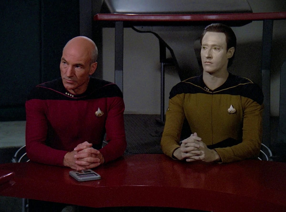 A picture of two character from the TV show Star Trek The Next Generation.  The characters are Captain Jean-Luc Picard and Lt Commander Data.  This is a courtroom scene to determine the rights of synthetic life forms
