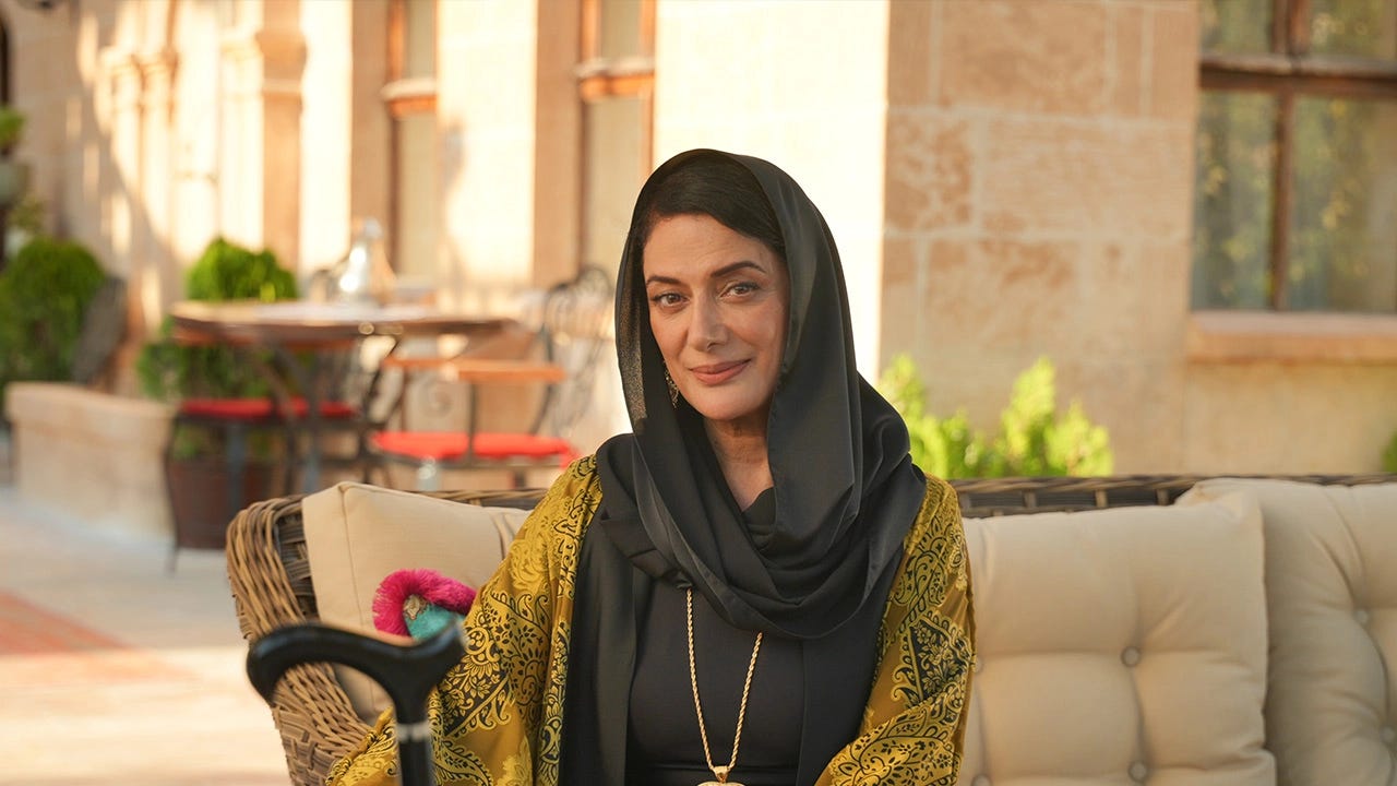 Veda Yurtsever, Halef: Köklerin Çağrısı dizisinde güçlü ve sakin duruşuyla karakterini yansıtırken, açık havada otururken görülüyor.