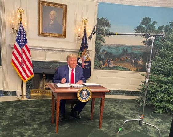 Donald Trump sits behind a little bitty desk to sign something, with a big boom microphne hanging down from a stand that wasn't visible on air