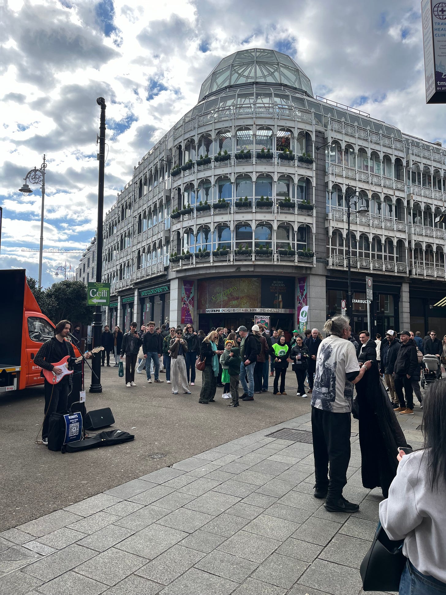 Photo of Grafton Street leading into St. Stephen's Green showing a busker playing guitar and a crowd of people watching Photo of Grafton Street leading into St. Stephen's Green showing a busker playing guitar and a crowd of people watching
