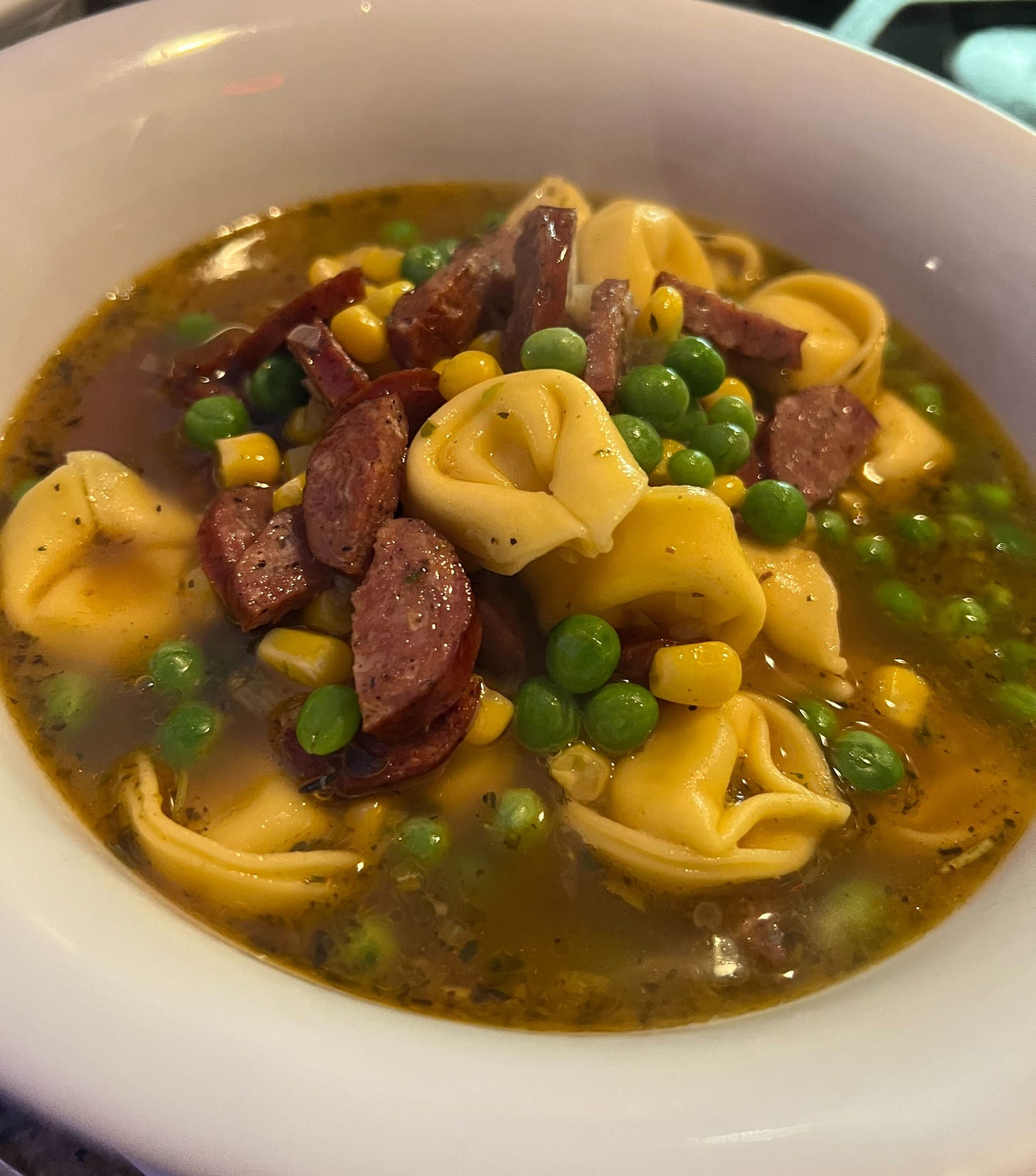 tortellini soup with peas, corn and sausage in a white bowl tortellini soup with peas, corn and sausage in a white bowl