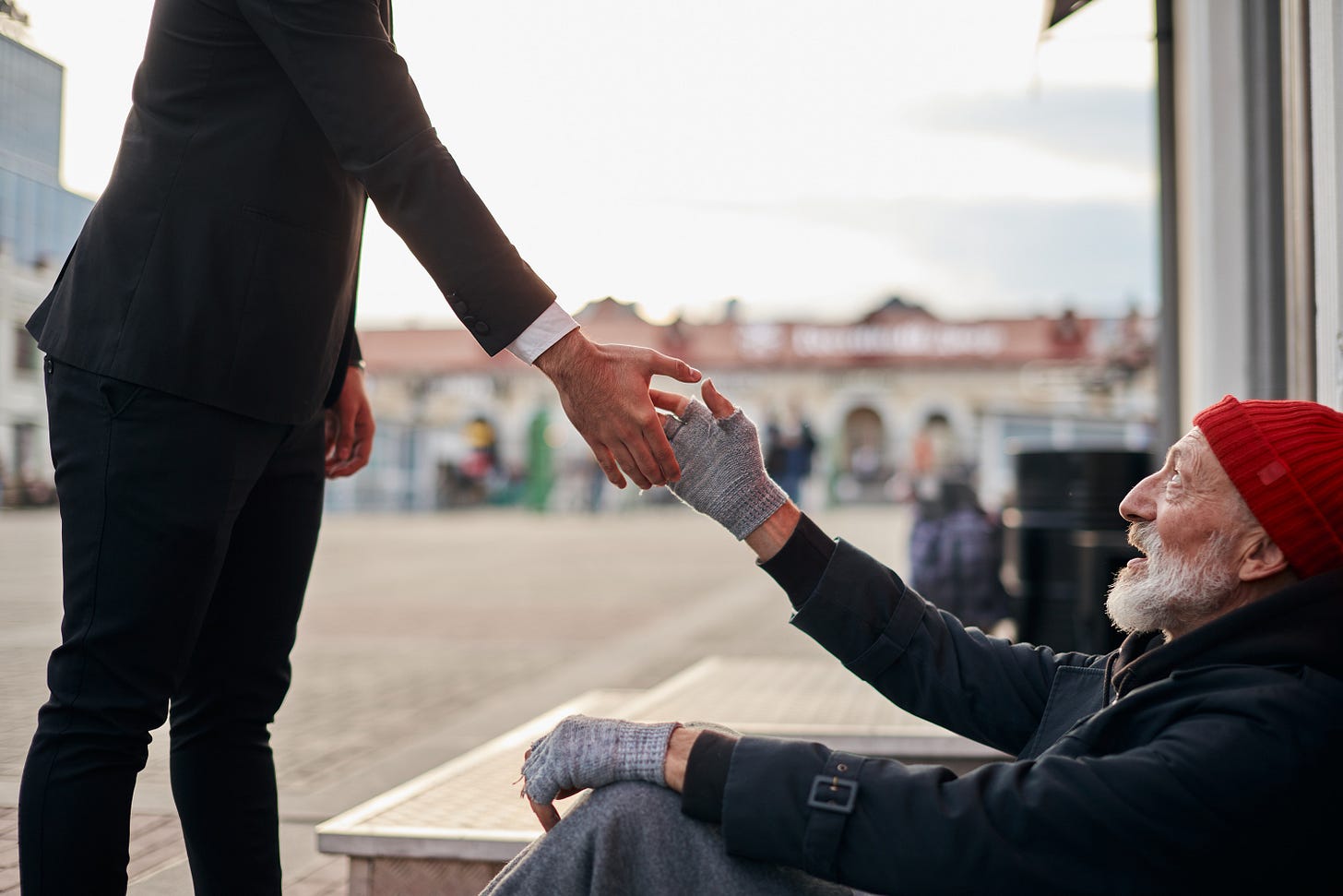 Man in suit offering his hand to an unhoused man on the street