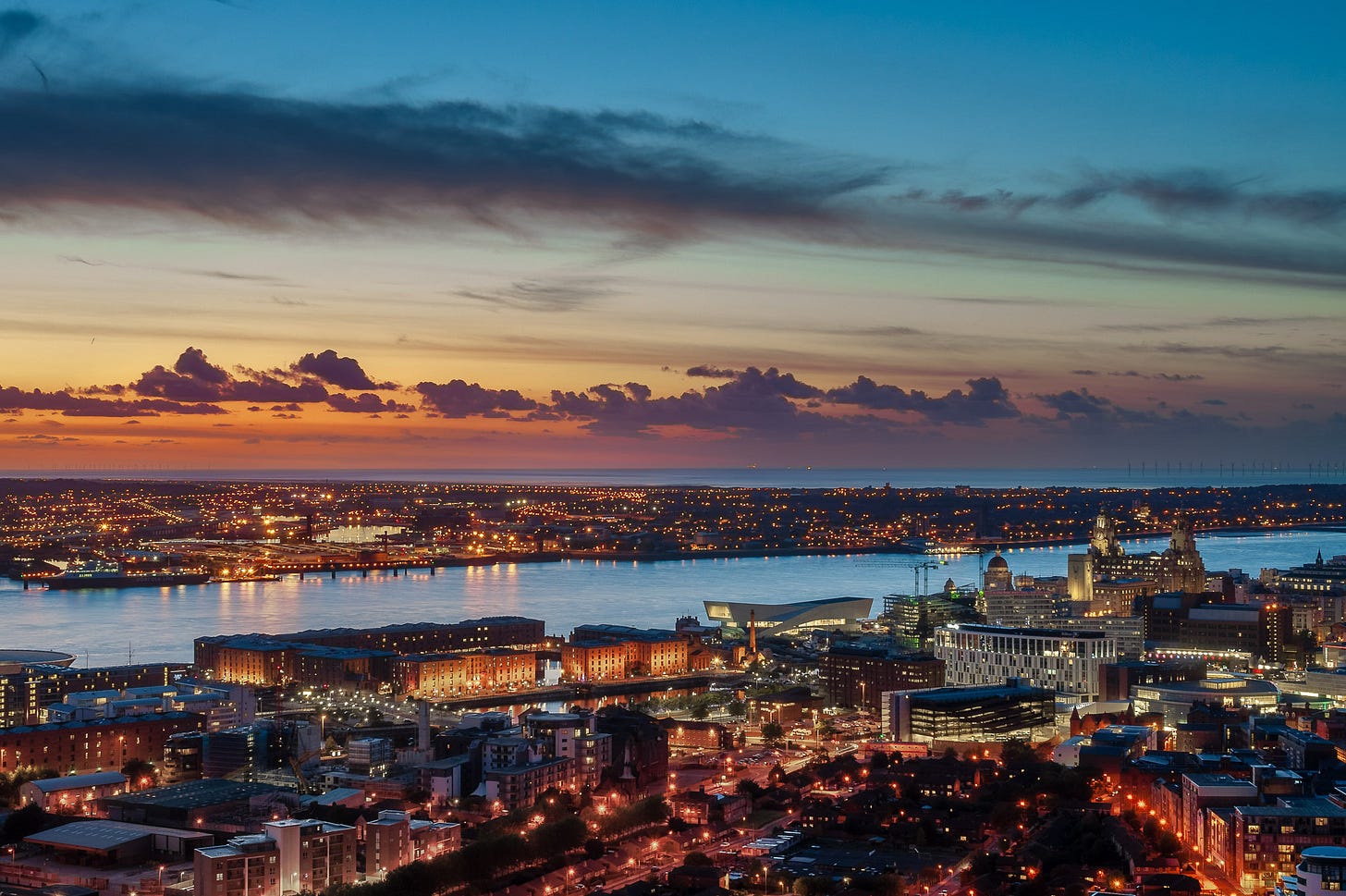 Dusk. The lights of the city are on. This is the Liverpool waterfront from the edge of the arena to Liver Building including the Royal Albert Dock, Museum of Liverpool and the 3 Graces.
