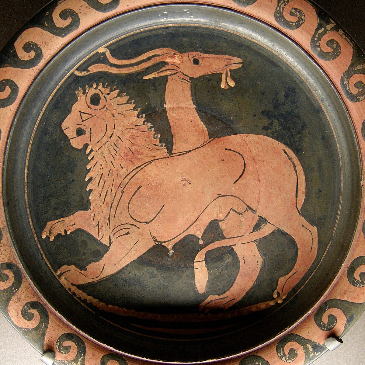 Ancient Apulian pottery plate: charcoal with red clay-colored images in relief. The plate has a wave-like border with an image of a chimera in the center -- a beast in profile with the heads of a lion and a goat, with a live snake for the tail.