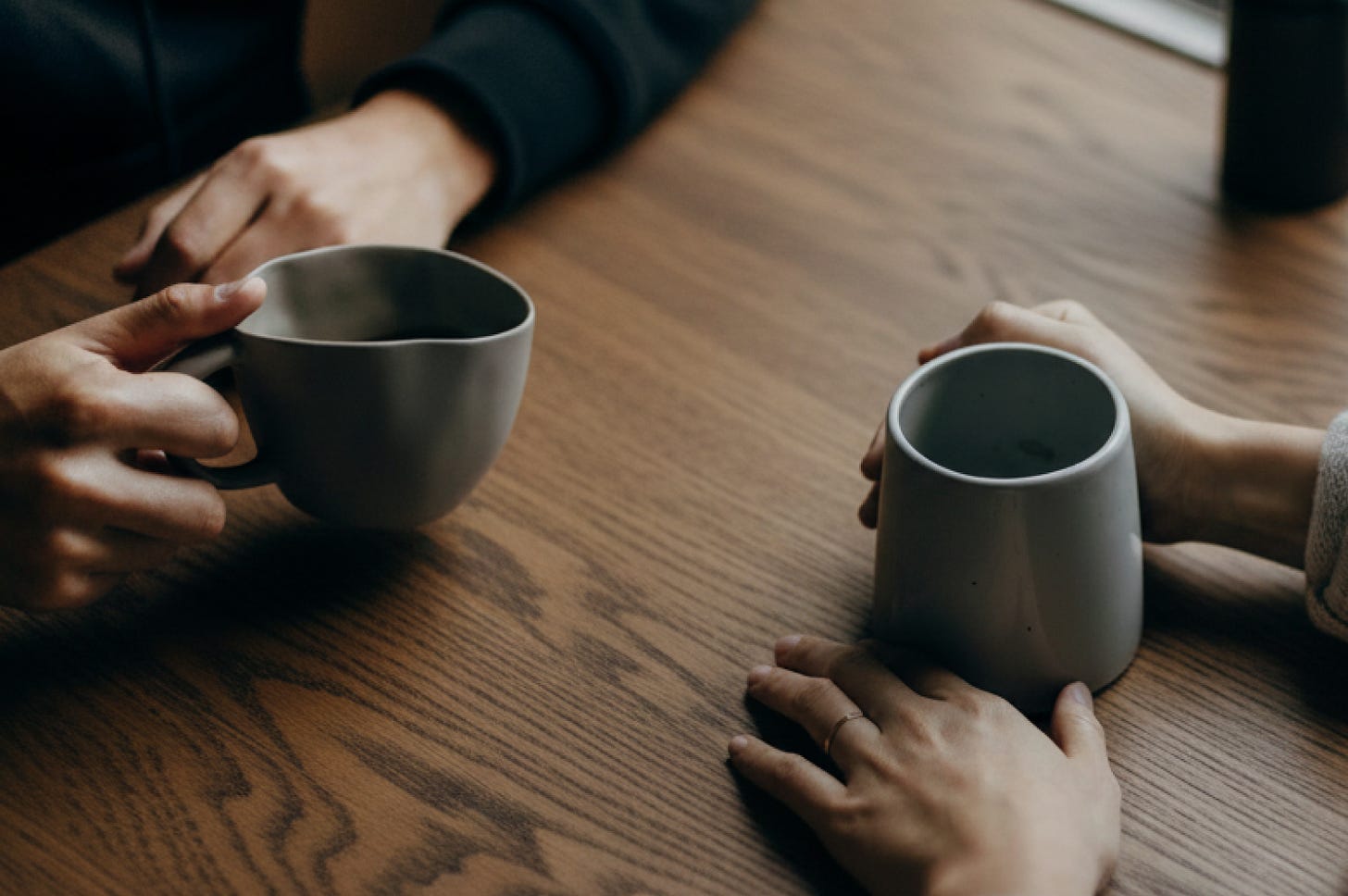 Two people sitting across from each other at a table, focused on two pairs of hands holding mugs