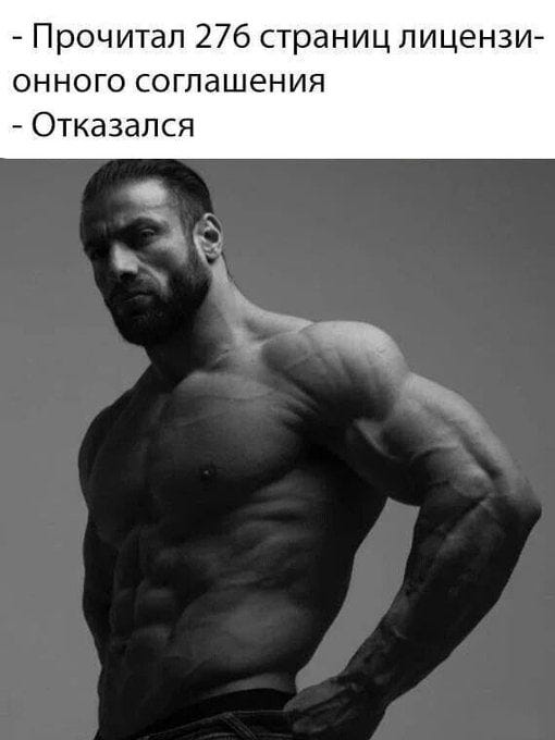 Dmitriy Dantes, a muscular man with a beard, stands shirtless, showcasing defined abdominal and arm muscles. He wears jeans and has a serious expression, posing with one hand on his hip.