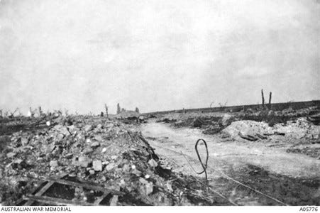 Black and white photograph of an unpaved road with debris from bombing of houses at Pozières, France in 1916.