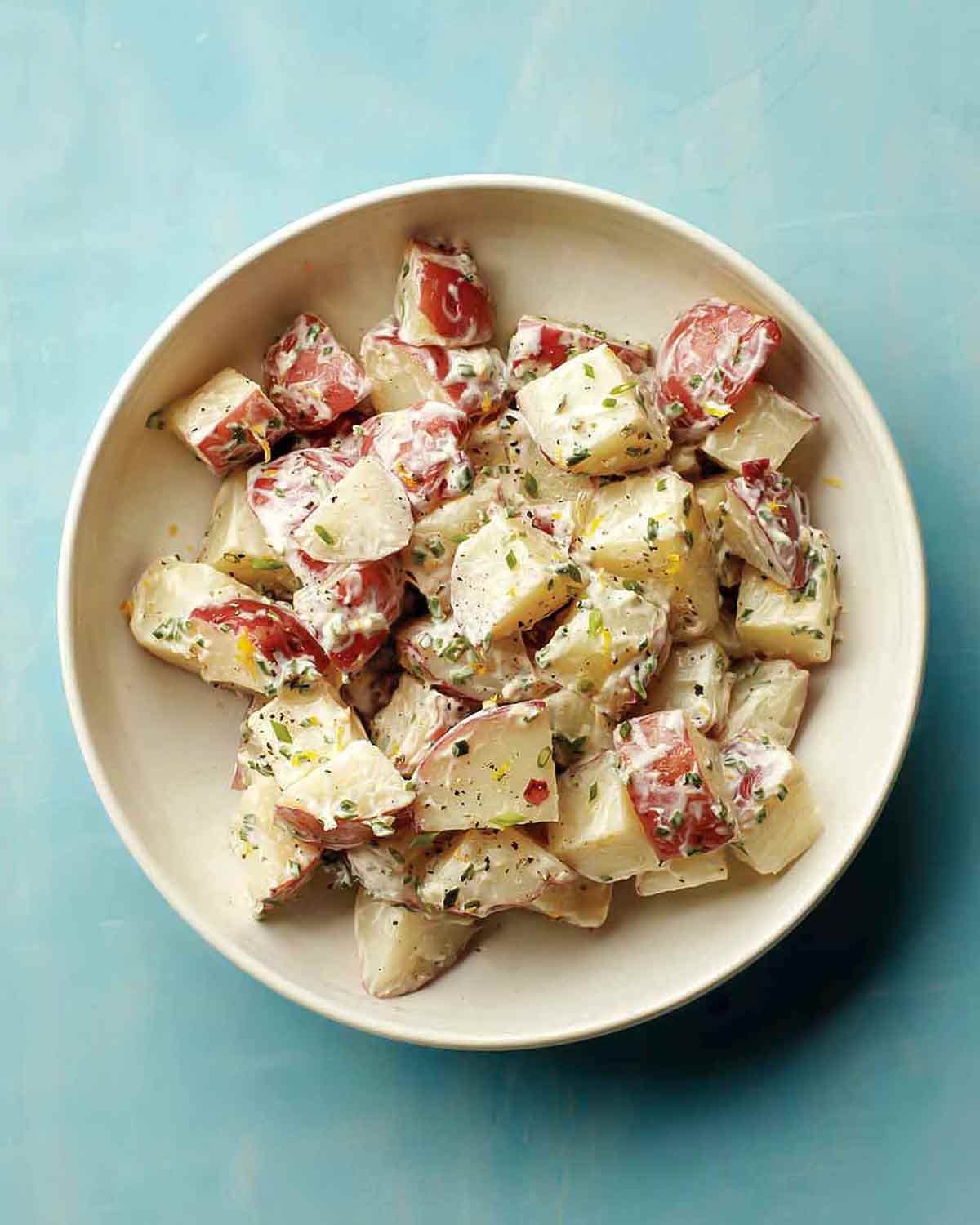 A close-up of creamy crème fraîche potato salad with red-skinned potatoes and fresh green herbs.