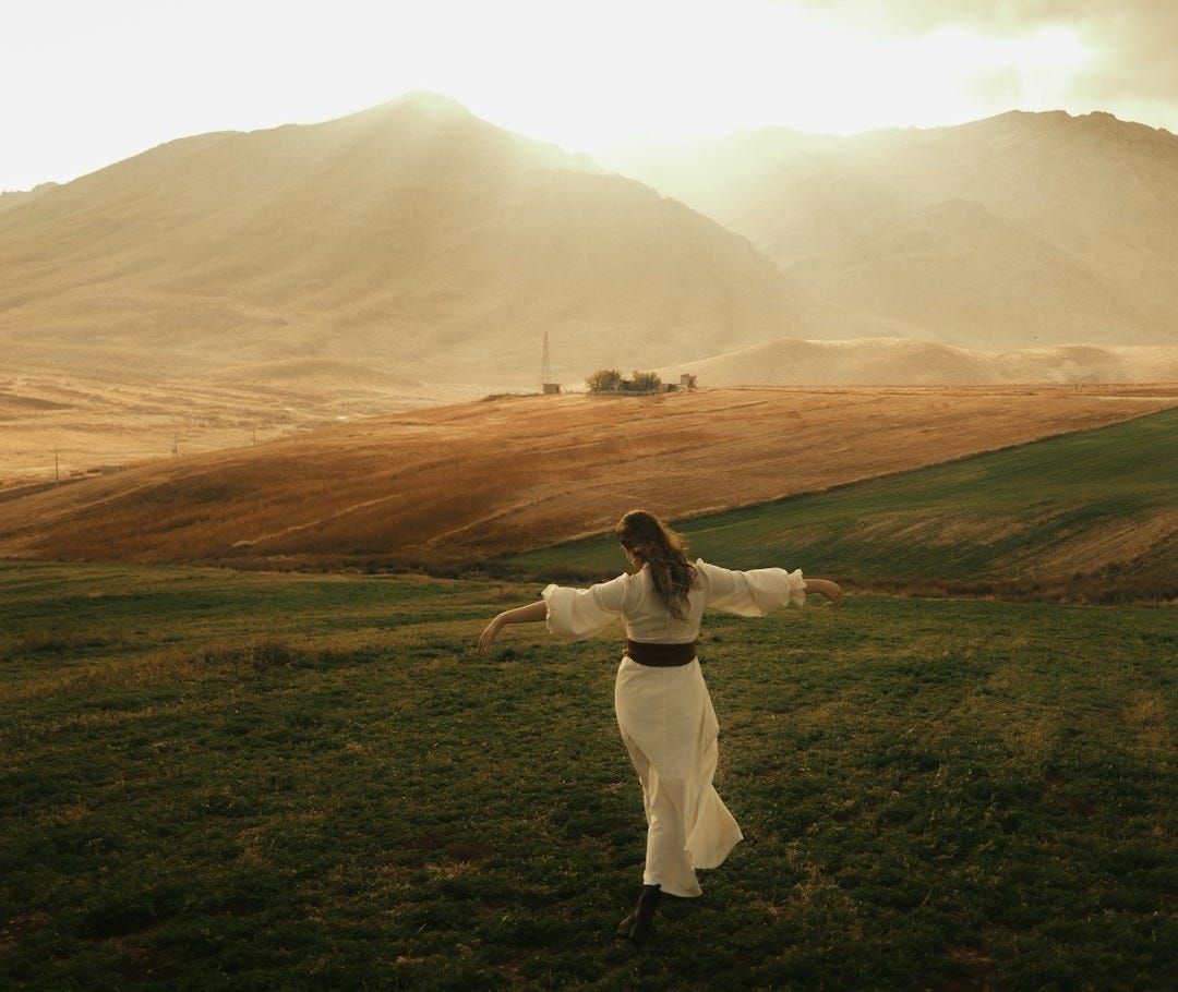 Woman in white dress in a grassy field with mountains Woman in white dress in a grassy field with mountains