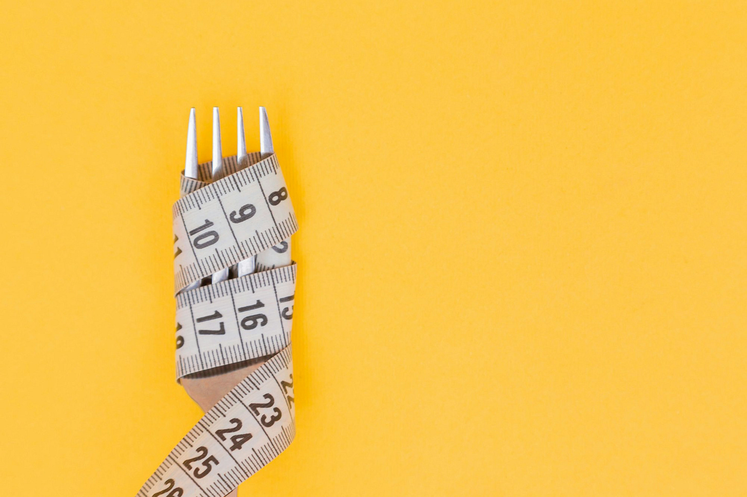 Iron fork and white measuring tape on a yellow background. Diet. Slimming. Obesity. Place for an inscription. Weight loss marathon. Advertising. Top view. The close plan. Iron fork and white measuring tape on a yellow background. Diet. Slimming. Obesity. Place for an inscription. Weight loss marathon. Advertising. Top view. The close plan.