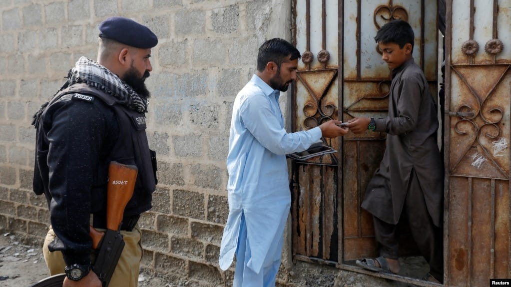 A worker from the National Database and Registration Authority, along with a police officer, verifies the identity cards of an Afghan citizen during a door-to-door search for undocumented Afghan nationals in Afghan Camp on the outskirts of Karachi, Pakistan, on Nov. 21, 2023.