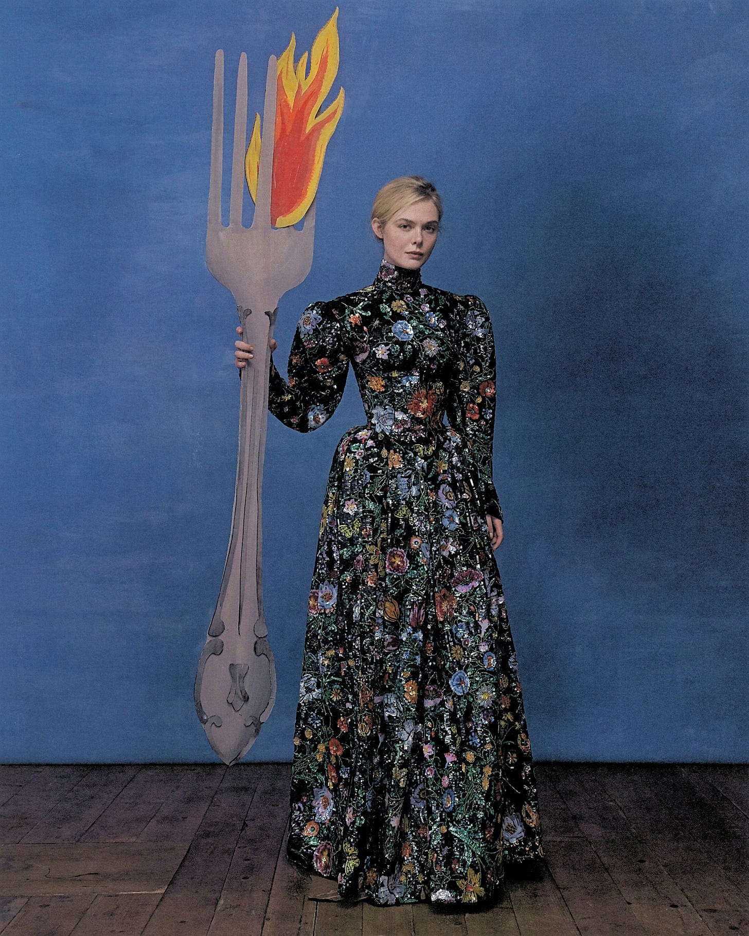 Elle Fanning shot by Szilveszter Mak&amp;amp;oacute;. Fanning is wearing a long sleeved Gucci gown with embroidered florals and is seen holding a large life-size cardboard cutout of a fork.