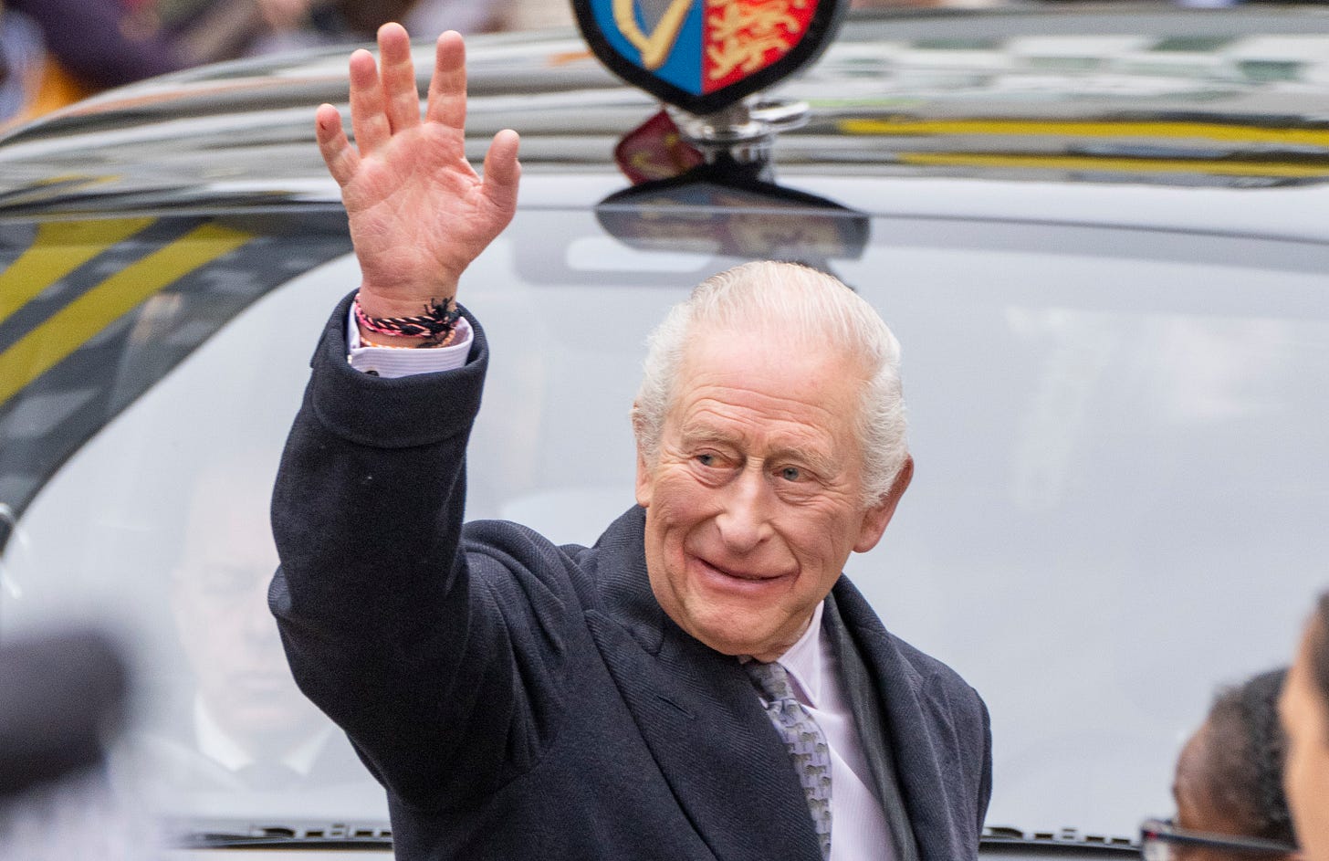 King Charles smiling and waving in front of a car