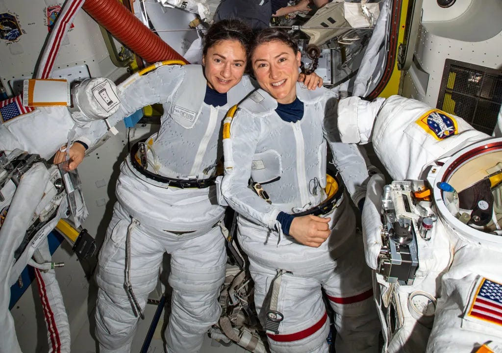 two women pose in spacesuits after completing a spacewalk