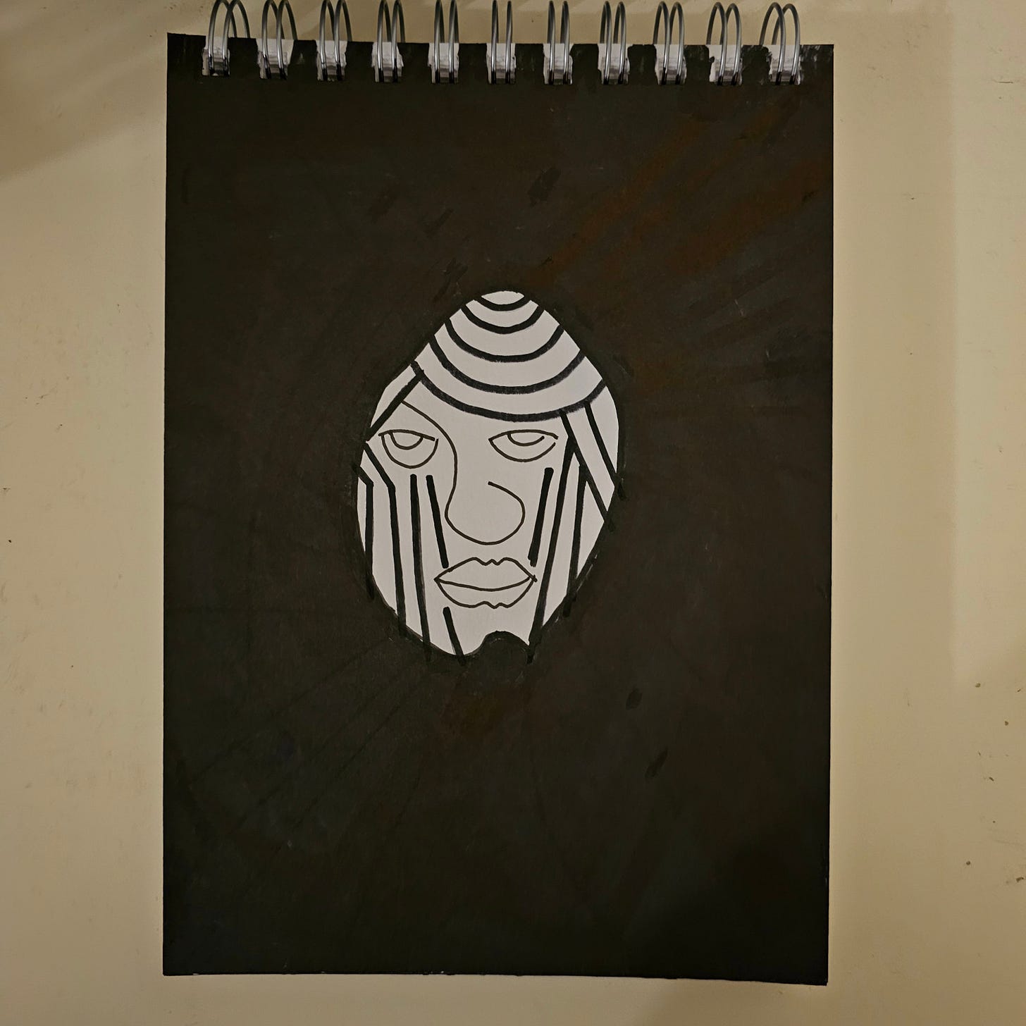 A stark black and white ink drawing of a floating, egg-shaped head against a solid black background. The face features heavy-lidded eyes, vertical lines running down the cheeks, and a series of concentric curves on the forehead, rendered in a graphic, neo-tribal style. A stark black and white ink drawing of a floating, egg-shaped head against a solid black background. The face features heavy-lidded eyes, vertical lines running down the cheeks, and a series of concentric curves on the forehead, rendered in a graphic, neo-tribal style.