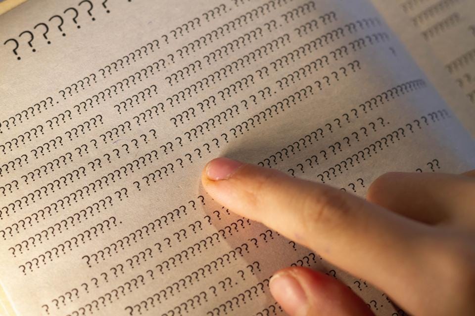 A person leads a finger on the lines in the book, but instead of letters only question marks on the page in the textbook