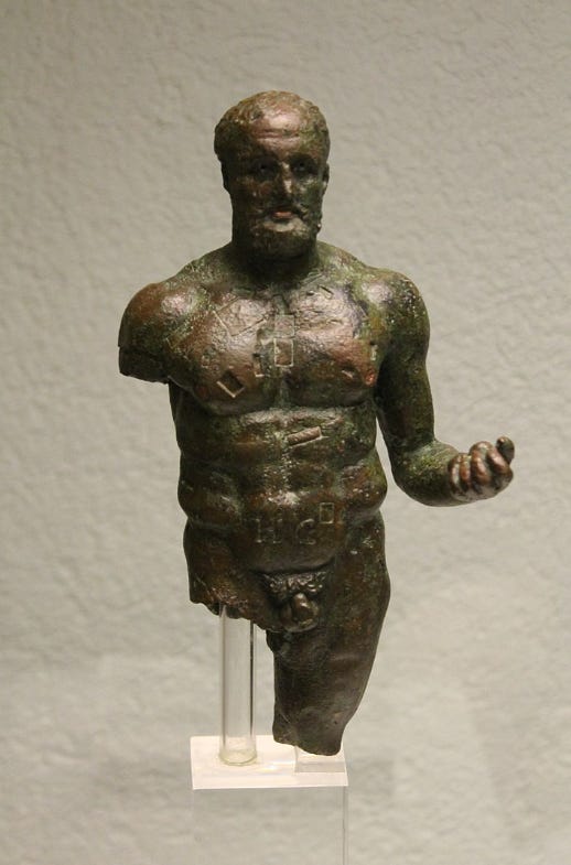 A bronze staue of a well muscled figure with short hair. His left arm is held forward and his elbow is bent and held close to his hip. His right arm is missing just below the shoulder as is his right leg.