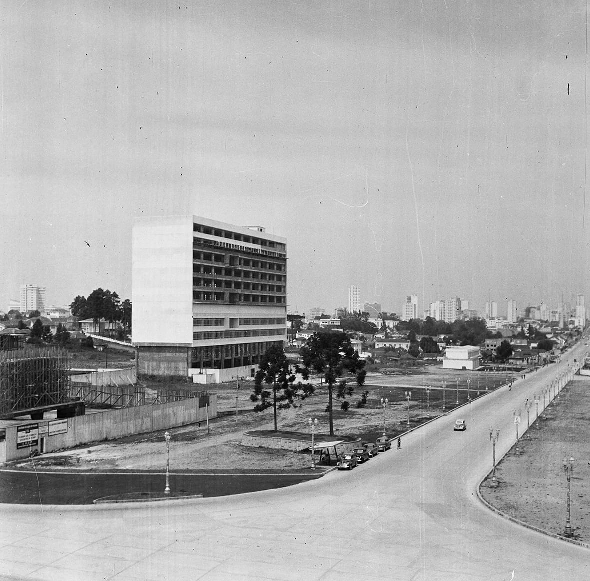 foto antiga da Avenida Cândido de Abreu, sem cores. uma via ampla, com prédios em construção à esquerda. duas araucárias. carros estacionados. ao fundo, paisagem do centro da cidade