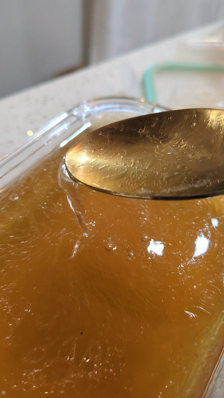 delicate teacup with asian art, with a small wooden spoonful of miso tare. Golden spoonful of fresh home made chicken and duck ramen broth spilling into glass container.