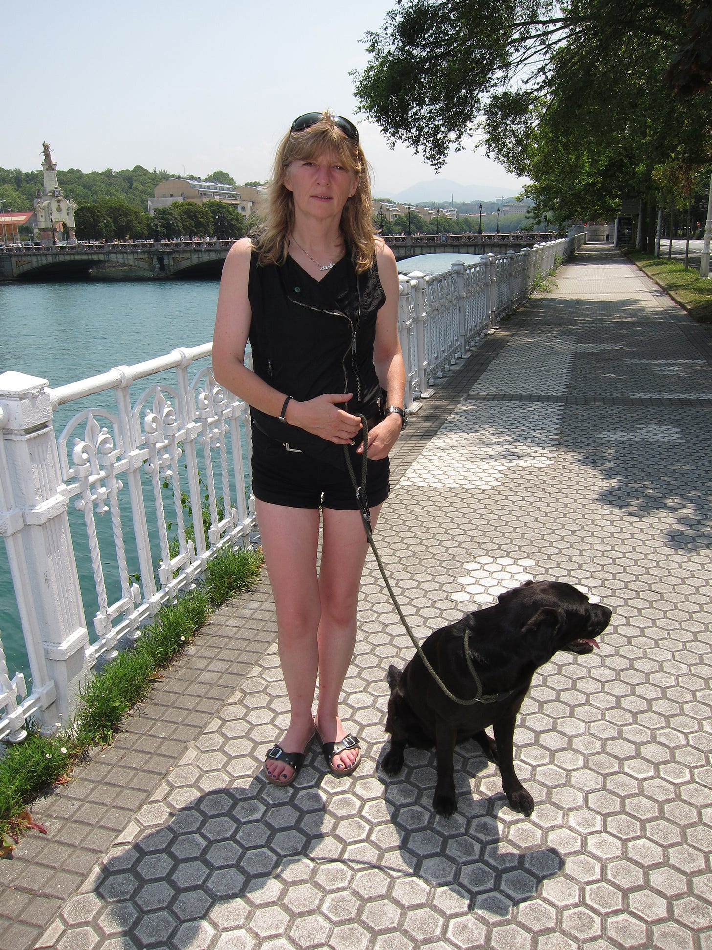 A woman with a black labrador in a path near a river