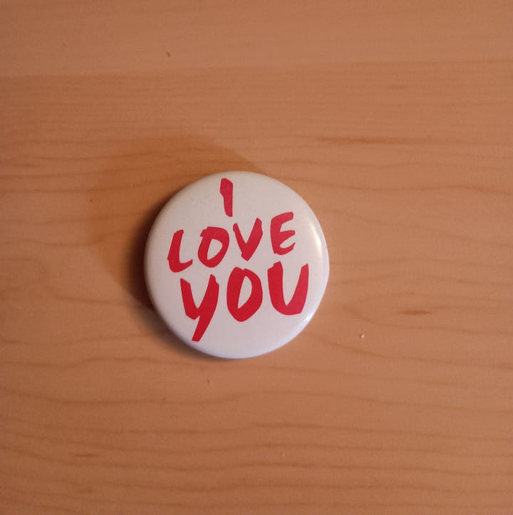 a pewter trojan warrior head side view and a white button with red words I love you