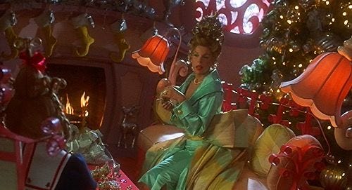 This may contain: a woman in a green dress sitting next to a christmas tree with presents on it