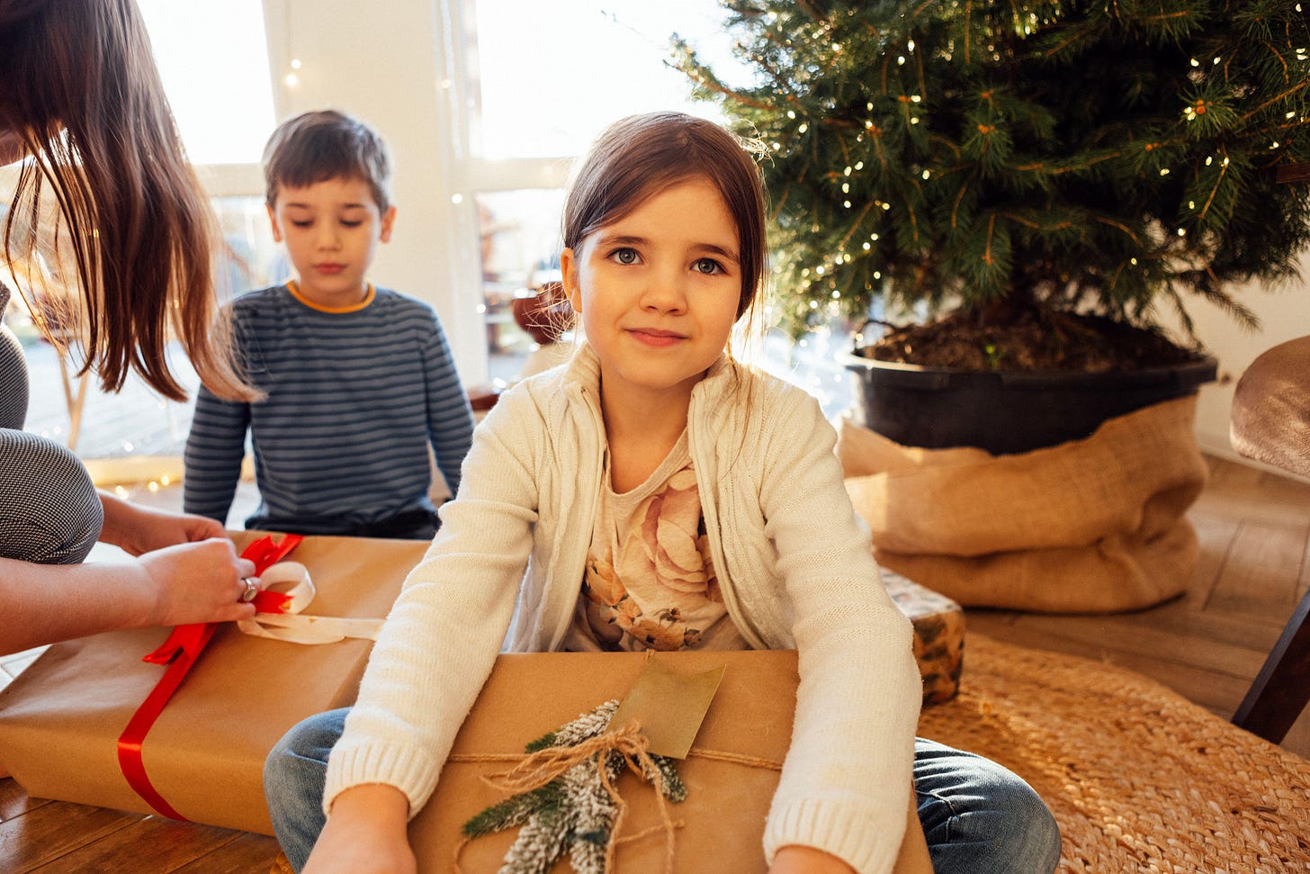Little girl and boy sitting next to christmas tree, opening presents