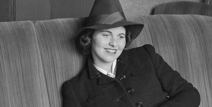 This may contain: a woman in a hat sitting on a couch