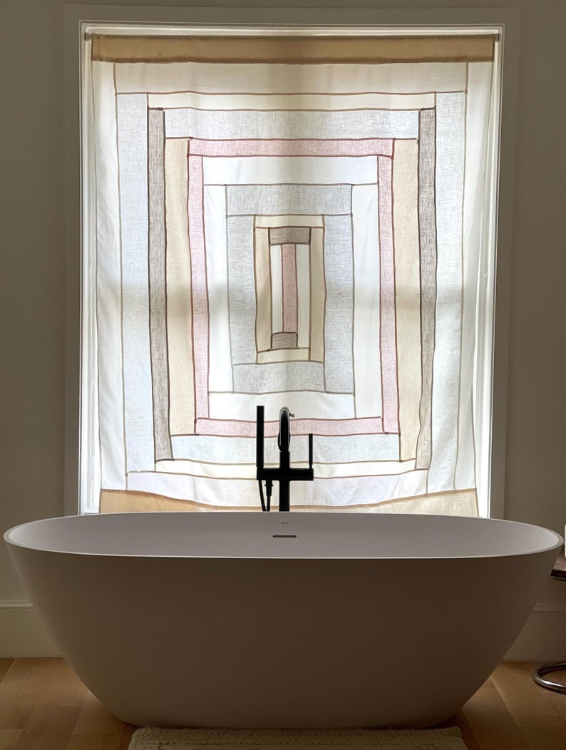 May include: A modern bathroom with a white oval bathtub and a black faucet. The window behind the tub has a decorative curtain with a geometric pattern in shades of white, pink, and brown.