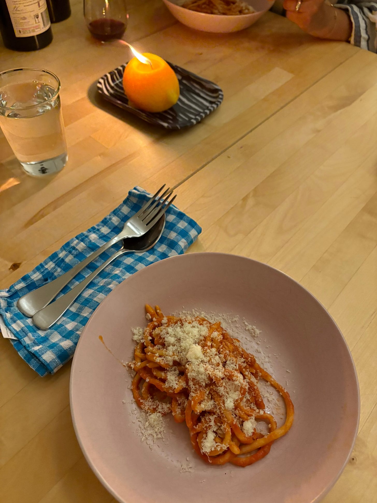 Bowl of pici with tomato vodka sauce. A lemon candle and wine in the background