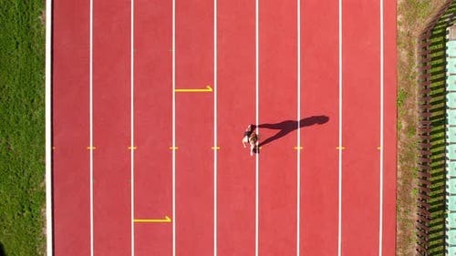 Aerial shot of a single runner on a red track, highlighted by a long shadow  and a yellow directional