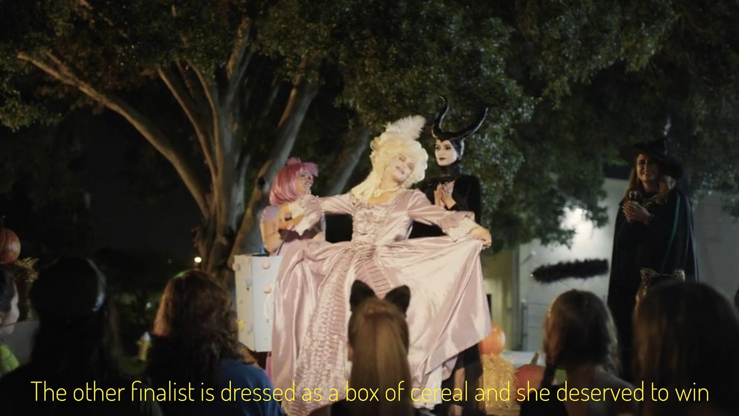 Gayle curtsying to the crowd in front of Vanessa and another lady, captioned "The other finalist is dressed as a box of cereal and she deserved to win"