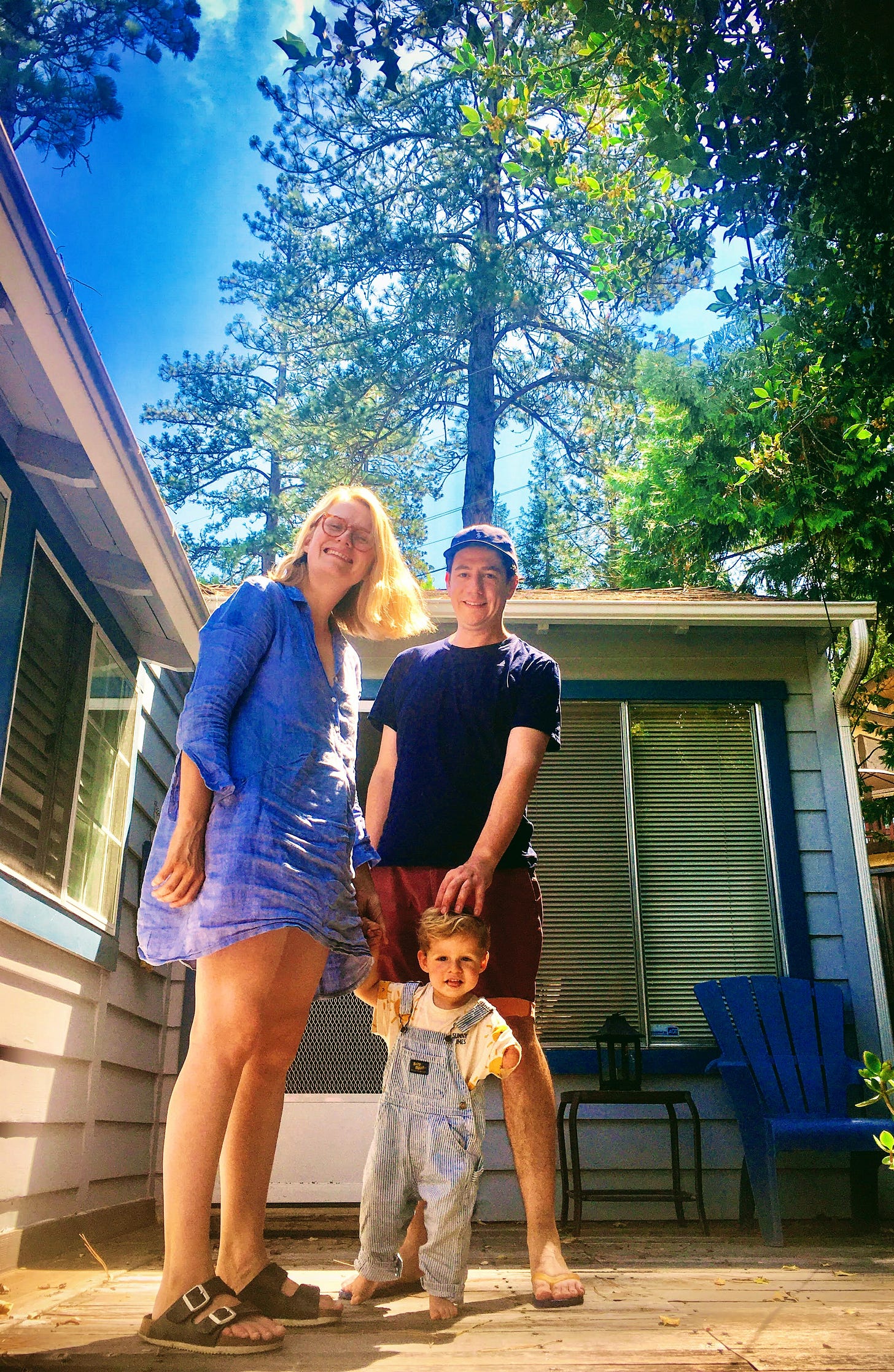 A man and woman stand in front of a house with their son.