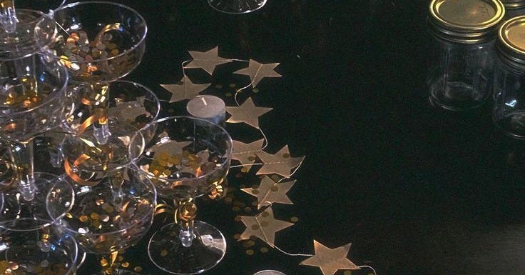 This may contain: several wine glasses and candles on a black table with gold stars scattered around the glass This may contain: several wine glasses and candles on a black table with gold stars scattered around the glass
