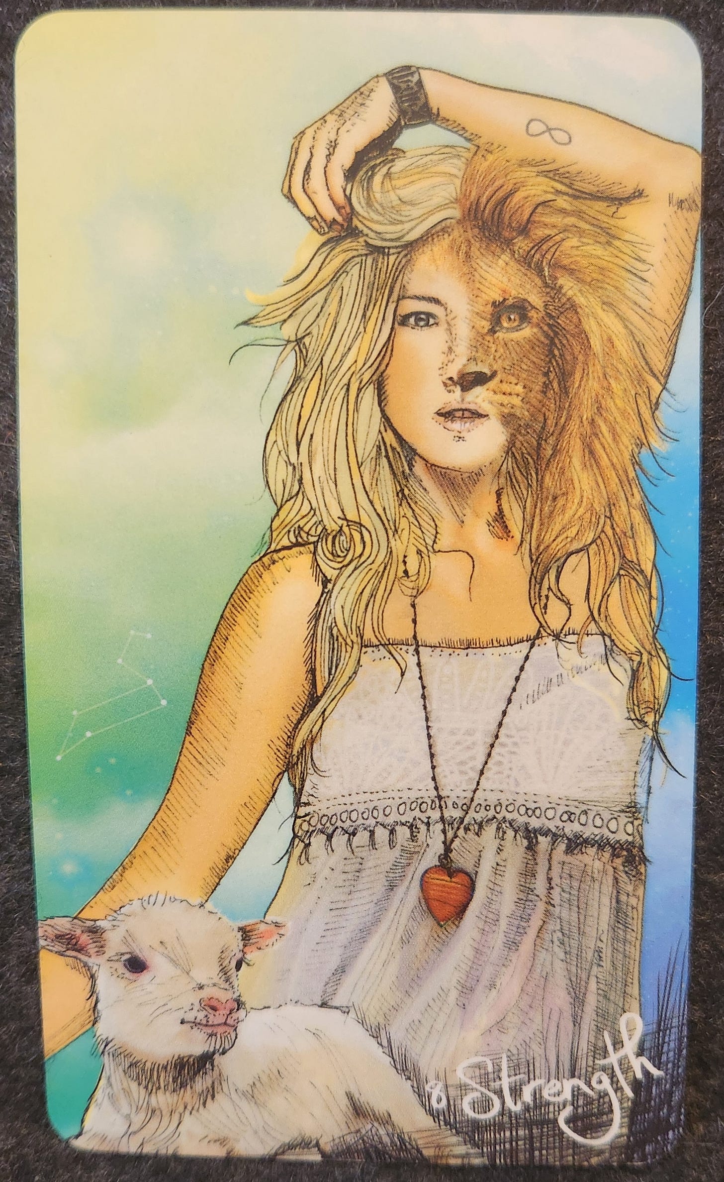 A tarot card labelled 8 Strength The Chariot. A woman with a half human and half lion face is sitting facing the camera. One arm is held above her head. She is wearing a long necklace with a red heart charm. She is holding a small white lamb in her lap. 