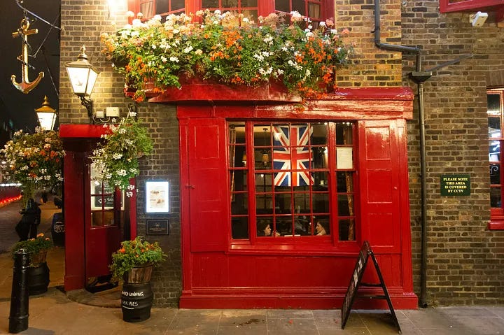 Photo by The Now Time on Unsplash of an British Pub with a bright red door and flower boxes