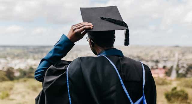 Rear view of male in academic gown, hood and cap, looking out over a distant landscape