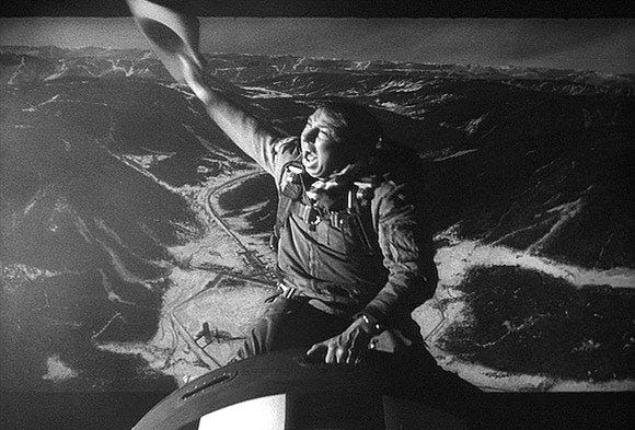 A film still of a man riding a bomb as one would a mechanical bull